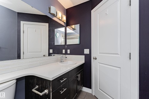 The bathroom features a vanity with a white countertop and a white sink, set against a dark wall - 35 675 Albany Way Nw, Edmonton, AB - Indoor Photo Showing Bathroom