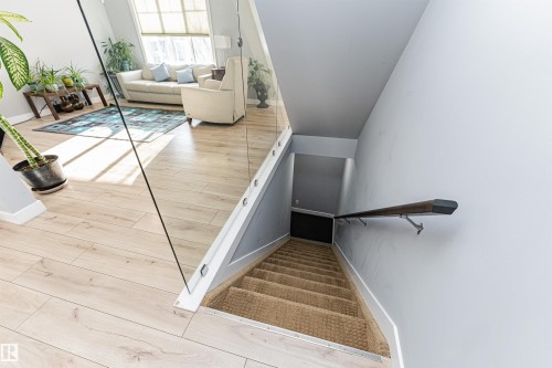The property features light-toned wood flooring, a glass stair railing, and a carpeted staircase with a dark wood handrail - 35 675 Albany Way Nw, Edmonton, AB - Indoor Photo Showing Other Room