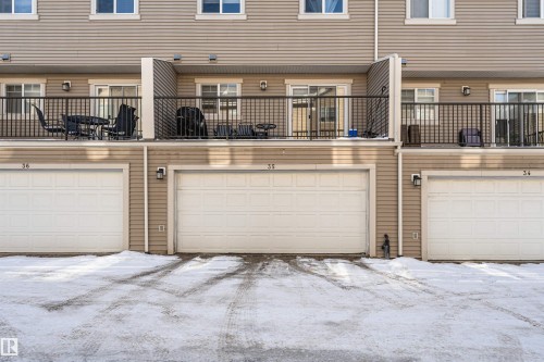 The property features an attached garage with a white garage door, an upper-level balcony with a black metal railing, and light-colored horizontal siding - 35 675 Albany Way Nw, Edmonton, AB - Outdoor With Balcony With Exterior