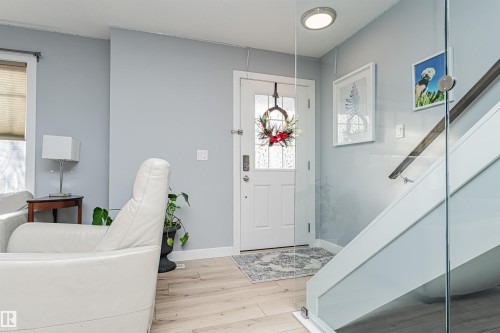 Entryway featuring light hardwood flooring, a white front door with decorative glass inserts, and a staircase with a clear glass railing and a wooden handrail - 35 675 Albany Way Nw, Edmonton, AB - Indoor