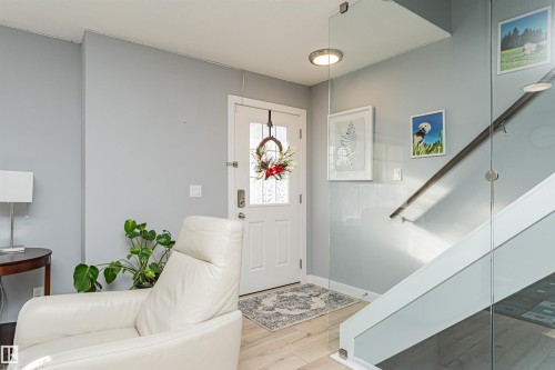 The property features a bright entryway with light wood flooring, a white front door with decorative glass inserts, and a contemporary glass panel staircase - 35 675 Albany Way Nw, Edmonton, AB - Indoor Photo Showing Other Room