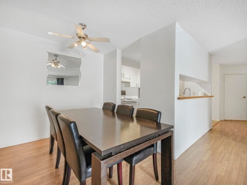 Dining area featuring wood-finish flooring, a ceiling fan with integrated lighting, and a pass-through to the kitchen with a wood countertop - 143 10636 120 Street Nw, Edmonton, AB - Indoor Photo Showing Dining Room