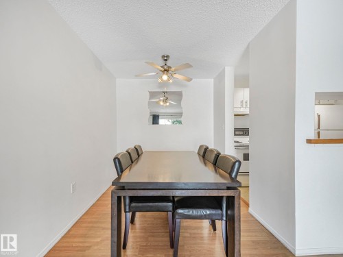 Dining area featuring wood-finish flooring, a ceiling fan with integrated lighting, and a pass-through window to the kitchen - 143 10636 120 Street Nw, Edmonton, AB - Indoor Photo Showing Dining Room