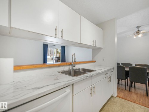 Kitchen featuring white cabinetry, a double basin stainless steel sink, and marble-look countertops - 143 10636 120 Street Nw, Edmonton, AB - Indoor Photo Showing Kitchen With Double Sink