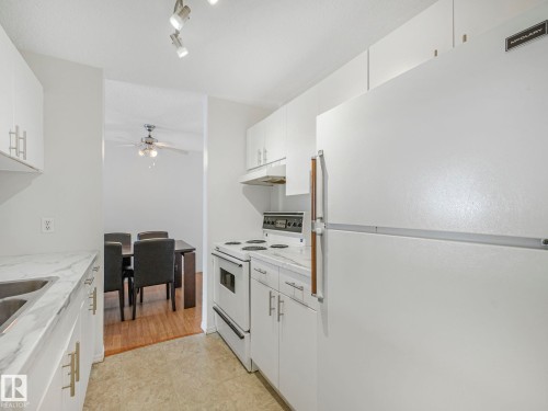 Kitchen featuring white cabinetry with brushed nickel hardware, white appliances, and track lighting - 143 10636 120 Street Nw, Edmonton, AB - Indoor Photo Showing Kitchen With Double Sink