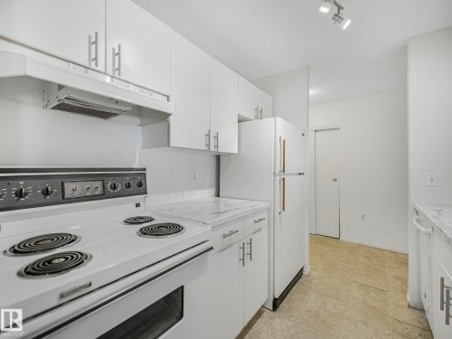 Kitchen featuring white cabinetry with silver-tone hardware, a white electric range with a range hood, a white refrigerator, and white countertops - 143 10636 120 Street Nw, Edmonton, AB - Indoor Photo Showing Kitchen