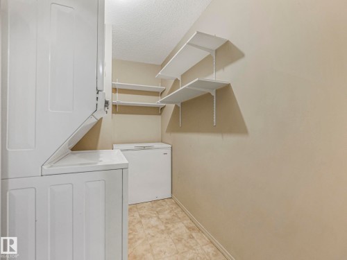 Dedicated utility area featuring a stacked washer and dryer, additional chest freezer, and wall-mounted shelving for organized storage - 143 10636 120 Street Nw, Edmonton, AB - Indoor Photo Showing Laundry Room