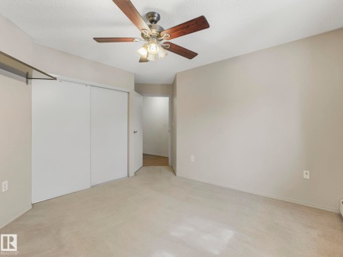 Carpeted room featuring a ceiling fan with integrated lighting, neutral wall paint, and double sliding closet doors - 143 10636 120 Street Nw, Edmonton, AB - Indoor Photo Showing Other Room