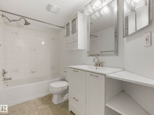 Bathroom featuring a white bathtub, ceramic wall tiling, and a vanity with an integrated sink - 143 10636 120 Street Nw, Edmonton, AB - Indoor Photo Showing Bathroom
