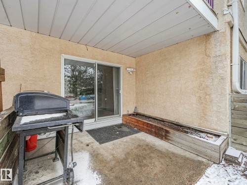 Covered concrete patio space featuring a sliding glass door entry, textured exterior wall, and a built-in planter box - 143 10636 120 Street Nw, Edmonton, AB - Outdoor With Exterior