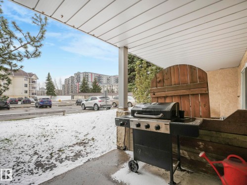 Covered patio featuring a wooden privacy screen, stucco exterior wall, and paved surface - 143 10636 120 Street Nw, Edmonton, AB - Outdoor With Deck Patio Veranda With Exterior