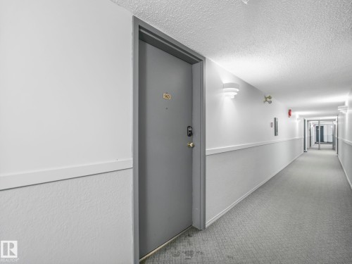 Hallway presenting a unit entry door with brass hardware and a unit number plaque - 143 10636 120 Street Nw, Edmonton, AB - Indoor Photo Showing Other Room