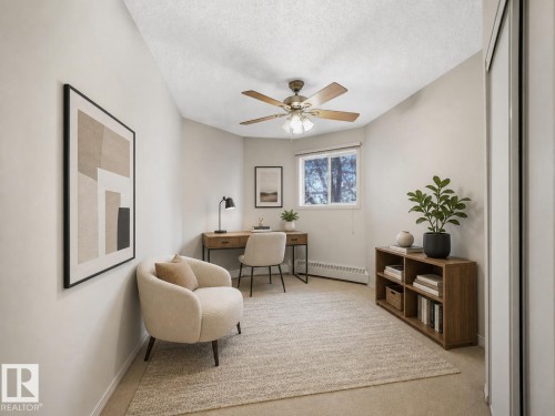 Neutral-toned room featuring a single window with outdoor scenery, ceiling fan with light fixture, light-colored carpeting, and white sliding closet doors - 143 10636 120 Street Nw, Edmonton, AB - Indoor Photo Showing Other Room