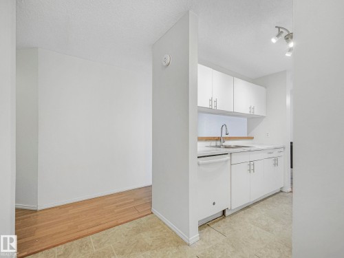 Compact kitchen featuring white cabinetry, a single basin sink with a gooseneck faucet, a white dishwasher, and light-colored countertops - 143 10636 120 Street Nw, Edmonton, AB - Indoor Photo Showing Kitchen
