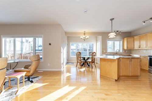 Open-concept living space featuring wood-finish flooring, a kitchen with light wood cabinetry and an island, a dining area with a chandelier, and ample natural light from multiple windows - 1915 126 Street, Edmonton, AB - Indoor