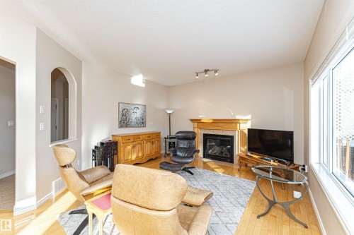 Living area featuring wood-finish flooring, a fireplace with a wood mantle and stone surround, and abundant natural light from a large window - 1915 126 Street, Edmonton, AB - Indoor Photo Showing Living Room With Fireplace