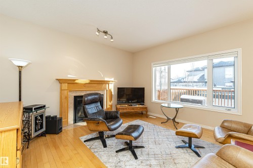 Living area featuring a fireplace with a light-colored mantel, hardwood flooring, and a large window - 1915 126 Street, Edmonton, AB - Indoor Photo Showing Other Room