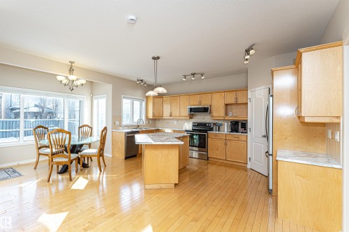 Bright kitchen featuring wood-finish flooring, light wood cabinetry, stainless steel appliances, a center island with a stone-finish countertop, and ample natural light through multiple windows - 1915 126 Street, Edmonton, AB - Indoor