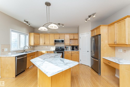 Spacious kitchen featuring light wood cabinetry, a central island with a white patterned countertop, stainless steel appliances, a tile backsplash, and wood-finish flooring - 1915 126 Street, Edmonton, AB - Indoor Photo Showing Kitchen With Double Sink