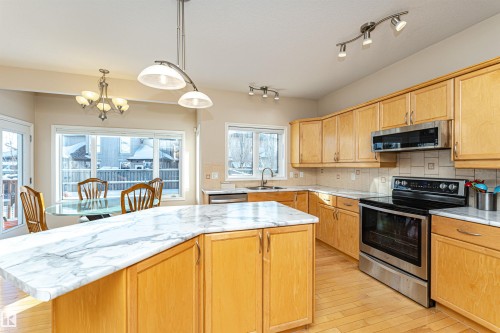 Kitchen featuring a large island with a patterned countertop, wood-finish cabinetry, stainless steel appliances, and light wood-finish flooring - 1915 126 Street, Edmonton, AB - Indoor Photo Showing Kitchen