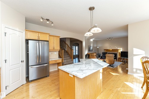 Open-concept kitchen featuring a central island with a white marble-patterned countertop, light wood cabinetry, stainless steel refrigerator, and wood-finish flooring - 1915 126 Street, Edmonton, AB - Indoor Photo Showing Kitchen