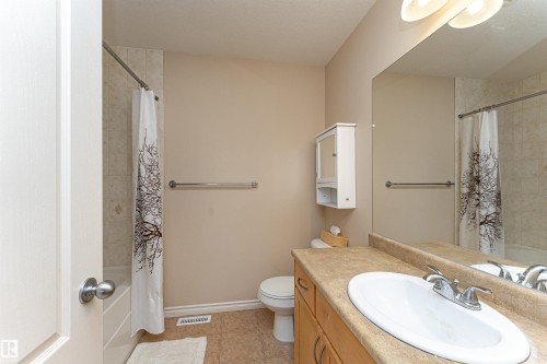 Full bathroom featuring a single vanity with wood cabinetry, a large wall-mounted mirror, a built-in medicine cabinet, and a shower-over-tub combination with tile surround - 1915 126 Street, Edmonton, AB - Indoor Photo Showing Bathroom