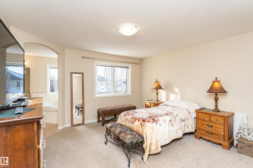 Carpeted bedroom featuring neutral-toned walls, a large window, and an arched doorway leading to a tiled bath area with a built-in tub - 1915 126 Street, Edmonton, AB - Indoor Photo Showing Bedroom