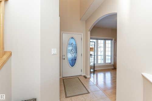 Entryway featuring a white door with an oval decorative glass insert, tiled flooring, and an arched opening leading to a room with large windows and wood-finish flooring - 1915 126 Street, Edmonton, AB - Indoor Photo Showing Other Room
