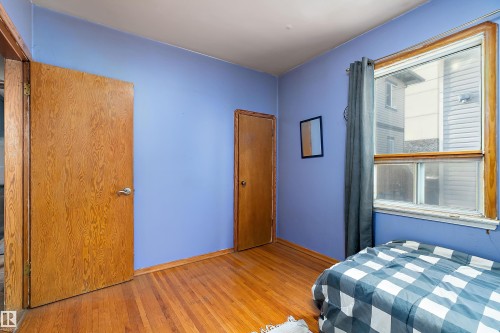 Room featuring wood-finish flooring, a window with wood trim, and two paneled doors with chrome hardware - 10124 88 Avenue, Edmonton, AB - Indoor Photo Showing Bedroom