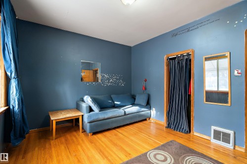 Hardwood flooring throughout this room featuring a window with natural wood trim, a built-in closet with privacy curtain, a wall-mounted mirror, and a floor vent - 10124 88 Avenue, Edmonton, AB - Indoor