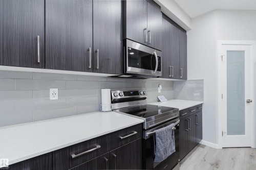 Modern kitchen featuring dark wood-finish cabinetry with stainless steel hardware, light-toned countertops, and a subway tile backsplash - 343 Edgemont Drive, Edmonton, AB - Indoor Photo Showing Kitchen