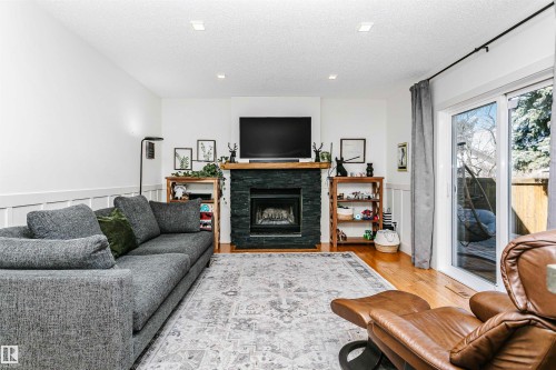 Living room featuring wood-finish flooring, a fireplace with a stacked stone facade and wood mantle, recessed lighting, and white wainscoting - 17820 57 Avenue, Edmonton, AB - Indoor Photo Showing Living Room With Fireplace
