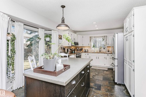 Kitchen featuring a central island with a solid surface countertop, white cabinetry with dark hardware, stainless steel appliances, slate-finish flooring, and recessed lighting - 17820 57 Avenue, Edmonton, AB - Indoor Photo Showing Kitchen