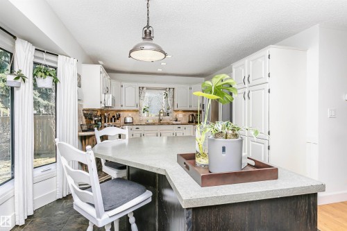 Kitchen featuring a large island with a composite countertop and dark wood-finish base, pendant lighting, white upper and lower cabinetry, and a bay window - 17820 57 Avenue, Edmonton, AB - Indoor Photo Showing Other Room