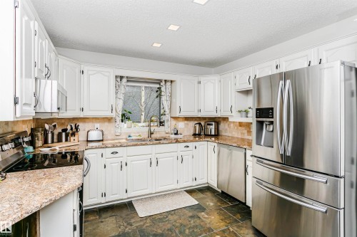 Kitchen featuring white cabinetry, stone-finish countertops, stainless steel appliances, and dark tile flooring - 17820 57 Avenue, Edmonton, AB - Indoor Photo Showing Kitchen With Double Sink
