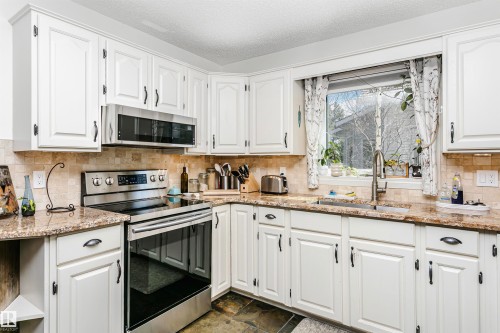Kitchen featuring white cabinetry, granite-finish countertops, stainless steel appliances, a tiled backsplash, and a window above the sink - 17820 57 Avenue, Edmonton, AB - Indoor Photo Showing Kitchen