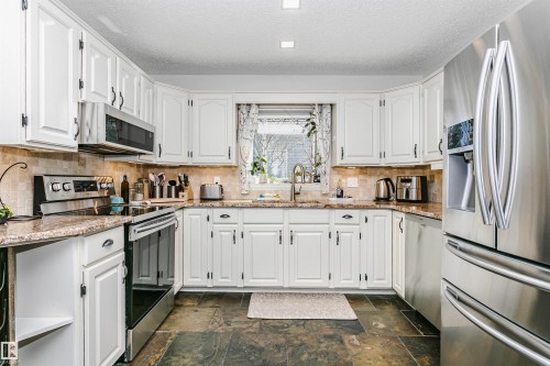 U-shaped kitchen featuring white cabinetry with black hardware, stainless steel appliances, stone countertops, and a tile backsplash - 17820 57 Avenue, Edmonton, AB - Indoor Photo Showing Kitchen