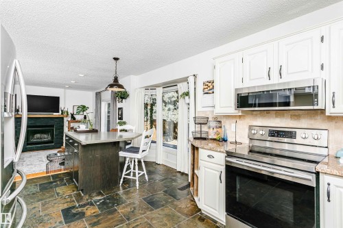 Kitchen featuring slate flooring, white cabinetry, stainless steel range and microwave, light granite countertops, and a stone tile backsplash - 17820 57 Avenue, Edmonton, AB - Indoor Photo Showing Kitchen