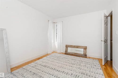 Light-filled room featuring hardwood-style flooring, white baseboards, and a window with sheer white curtains - 17820 57 Avenue, Edmonton, AB - Indoor