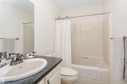 Bathroom featuring a fiberglass tub and shower combination, vanity with an integrated sink, dark countertop, and a tiled backsplash - 17820 57 Avenue, Edmonton, AB - Indoor Photo Showing Bathroom