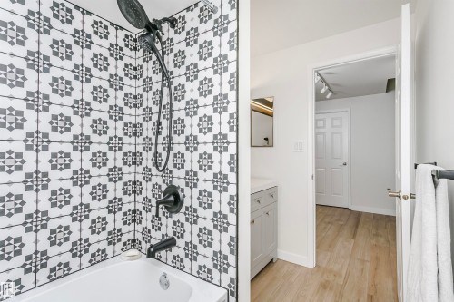 Tub and shower combination featuring black and white patterned tile surround, matte black fixtures, and a white soaking tub - 17820 57 Avenue, Edmonton, AB - Indoor Photo Showing Bathroom
