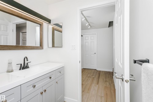 Bathroom vanity featuring a white countertop, gray shaker-style cabinetry, and a rectangular wood-framed mirror with integrated lighting - 17820 57 Avenue, Edmonton, AB - Indoor Photo Showing Other Room