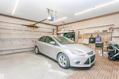 Attached garage featuring a panel garage door, concrete flooring, overhead fluorescent lighting, and built-in shelving - 17820 57 Avenue, Edmonton, AB - Indoor Photo Showing Garage