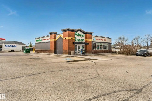 Commercial building featuring brick and stucco exterior, prominent storefront windows, a paved parking lot, and a visible business sign - 17820 57 Avenue, Edmonton, AB - Outdoor