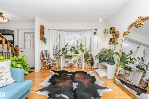 Hardwood flooring in a bright interior space featuring a decorative front door with transom window and a large bay window - 17820 57 Avenue, Edmonton, AB - Indoor Photo Showing Living Room