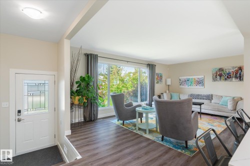 Expansive living area featuring large windows, wood-finish flooring, and a bright, open entry with a decorative glass panel door - 10339 36A Avenue, Edmonton, AB - Indoor