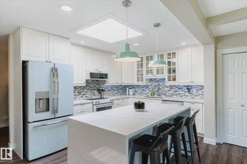 Modern kitchen featuring white cabinetry, a large center island with seating, a mosaic tile backsplash, recessed lighting, and a prominent skylight - 10339 36A Avenue, Edmonton, AB - Indoor Photo Showing Kitchen With Upgraded Kitchen