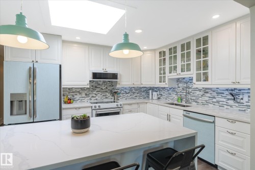 Kitchen featuring a central island with a light-toned countertop, white cabinetry, a skylight, a tile backsplash, and recessed lighting - 10339 36A Avenue, Edmonton, AB - Indoor Photo Showing Kitchen With Double Sink With Upgraded Kitchen