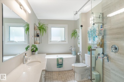 Bathroom featuring a white freestanding bathtub, large vanity with integrated sink, glass-enclosed shower, and dual windows - 10339 36A Avenue, Edmonton, AB - Indoor Photo Showing Bathroom