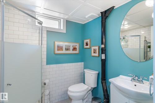 Bathroom featuring subway tile wainscoting, a glass-enclosed shower with frosted panel, a rectangular transom window, and a circular wall mirror above a vanity with integrated sink - 10339 36A Avenue, Edmonton, AB - Indoor Photo Showing Bathroom
